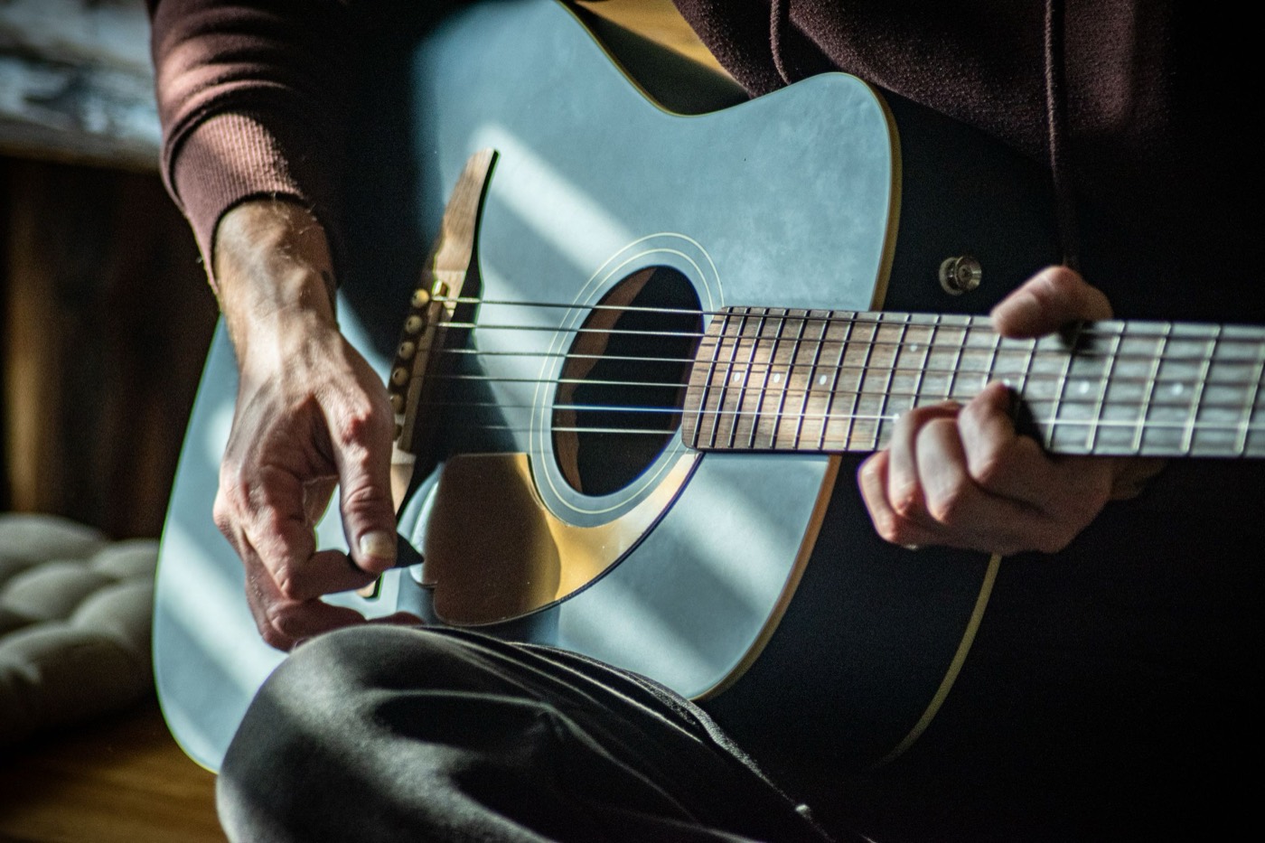 Hands picking an acoustic guitar in warm sunlight