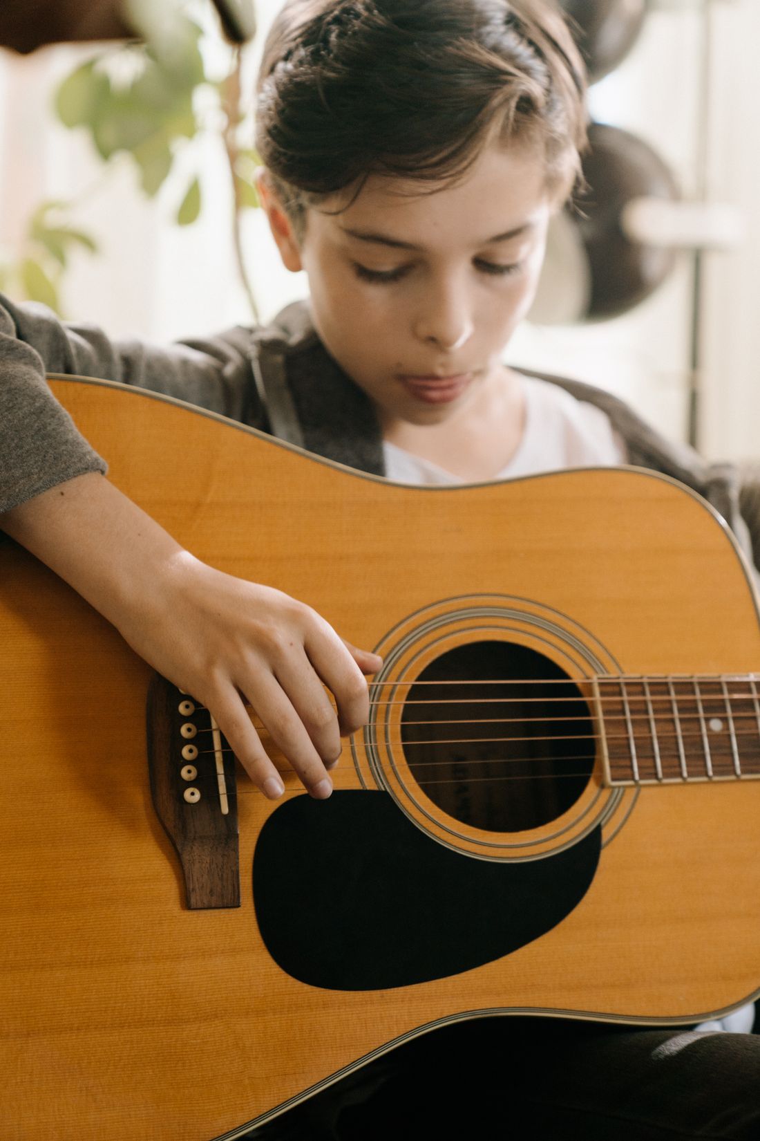 A young student concentrating while strumming an acoustic guitar