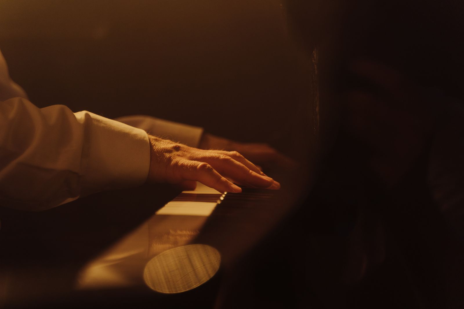 Hands resting on piano keys in warm low light